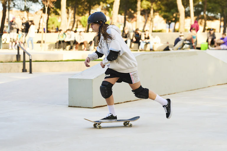 A girl in casual clothes riding a skateboard in a skate park.