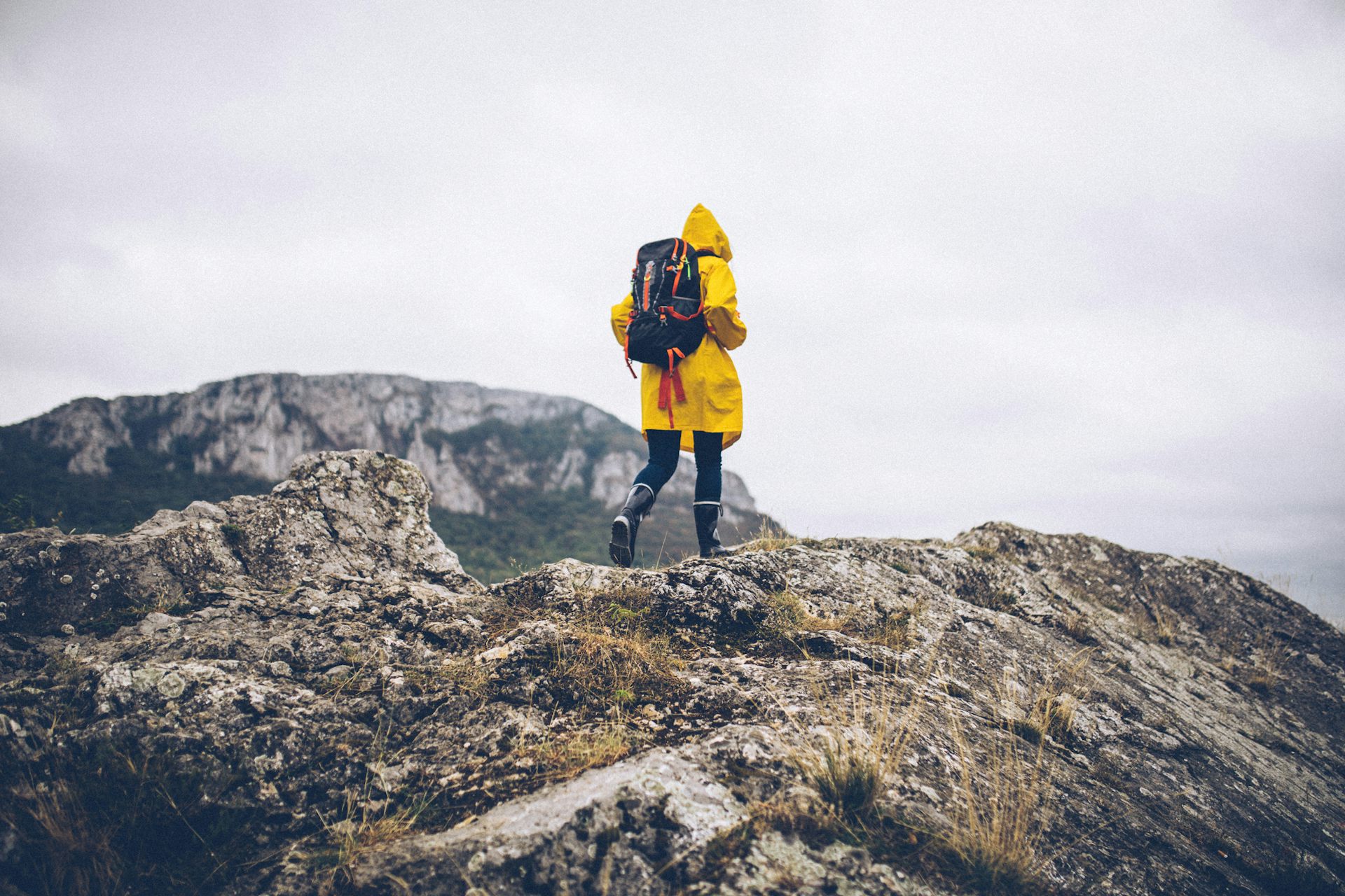 Young woman in a yellow raincoat hikes on a mountain.