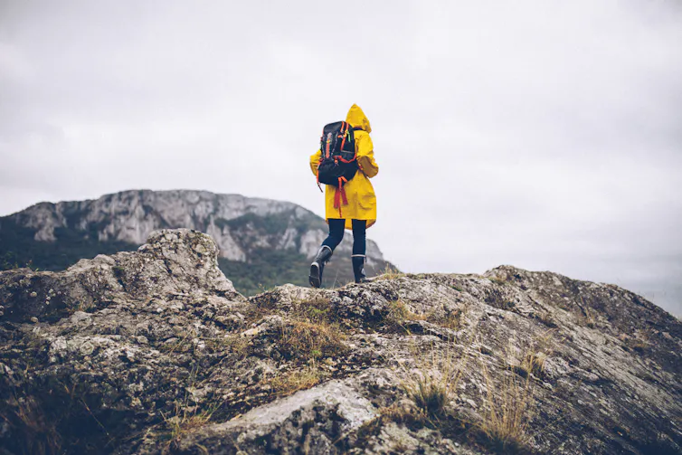 Young woman in a yellow raincoat hikes on a mountain.