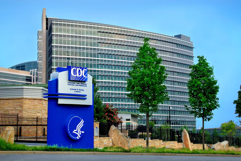 A large glass building with a blue sign in front of it that says CDC and depicts the agency's logo