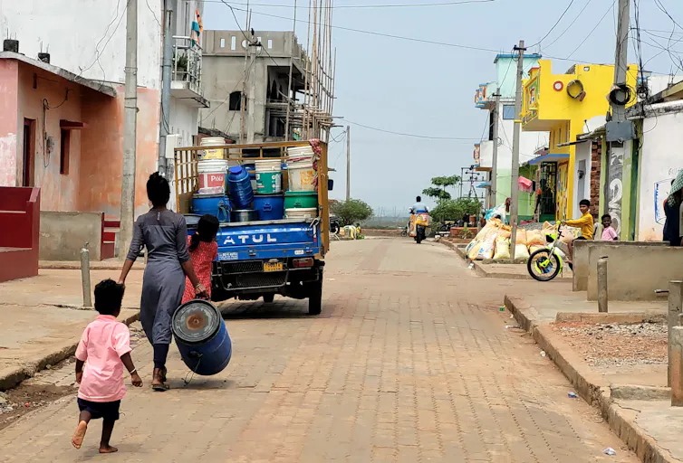 Woman carries water barrel on street in Indian village