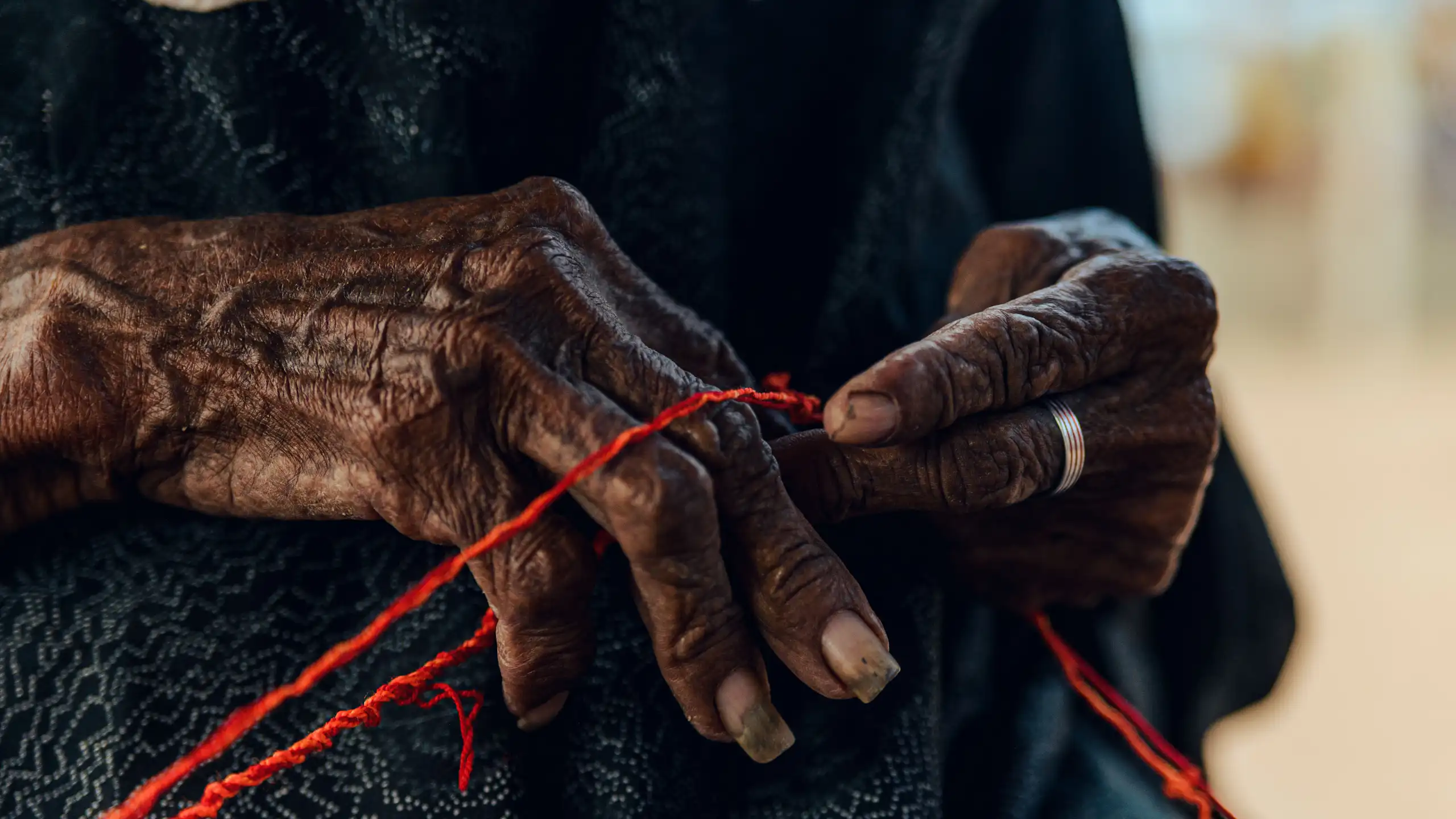 Detailed close-up of an elderly woman's hands crafting with red thread