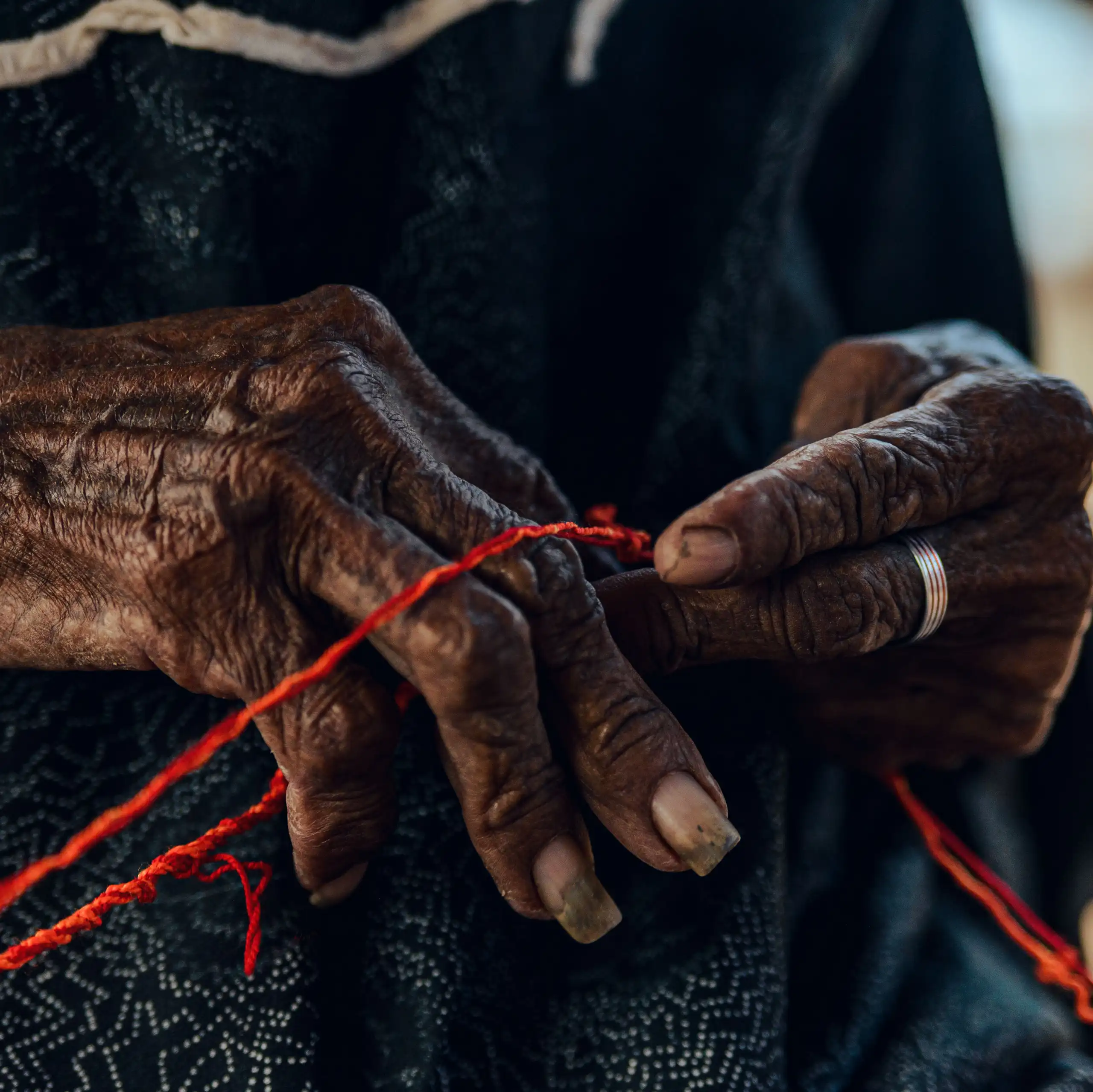 Detailed close-up of an elderly woman's hands crafting with red thread
