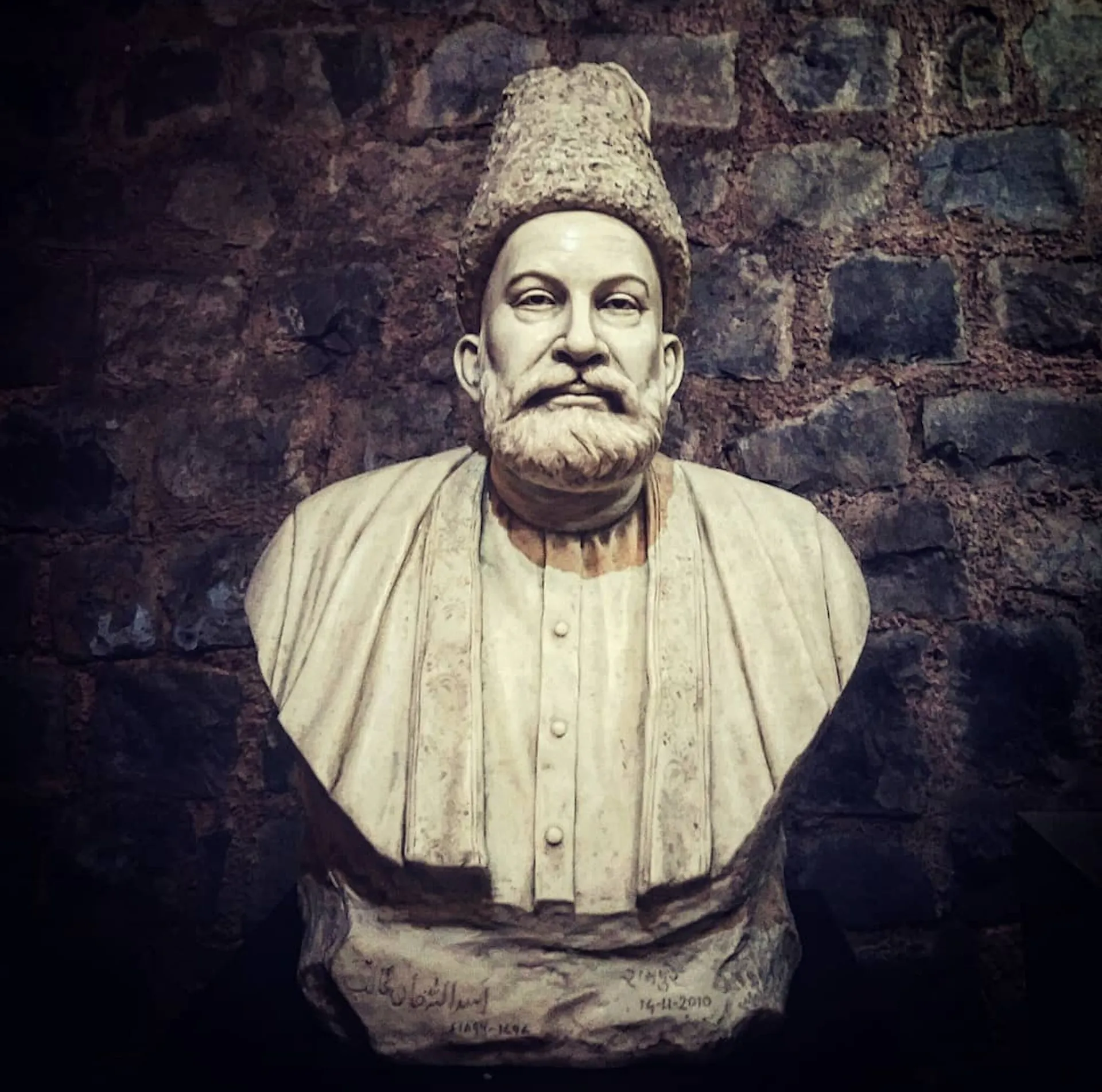 A stone bust of a man with a gray beard and mustache wearing a hat.