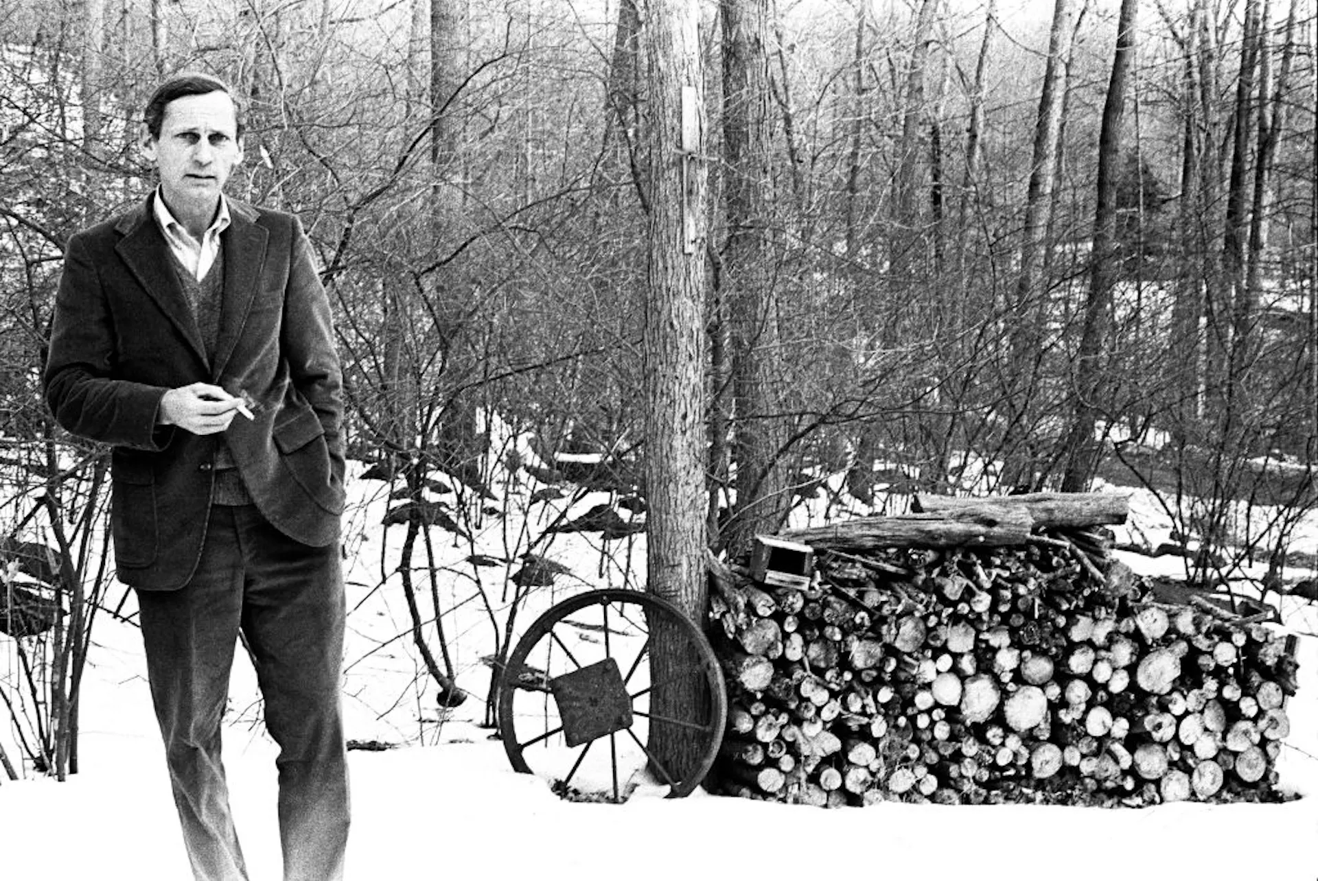 Black-and-white photo of middle-aged man standing in snowy woods, holding a cigarette.