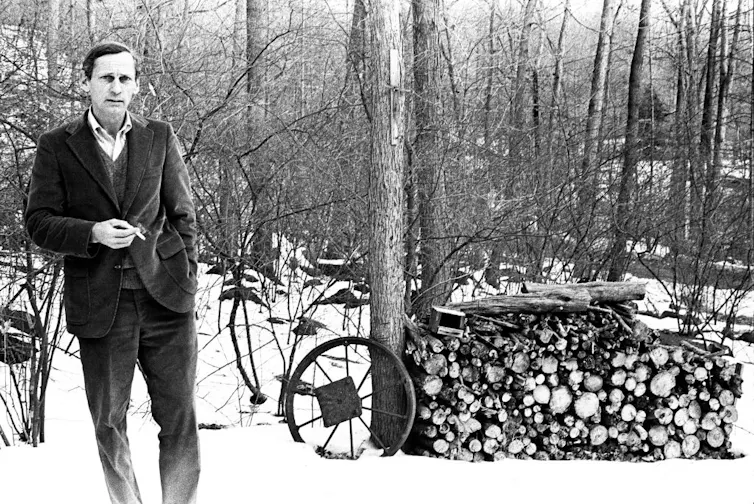 Black-and-white photo of middle-aged man standing in snowy woods, holding a cigarette.