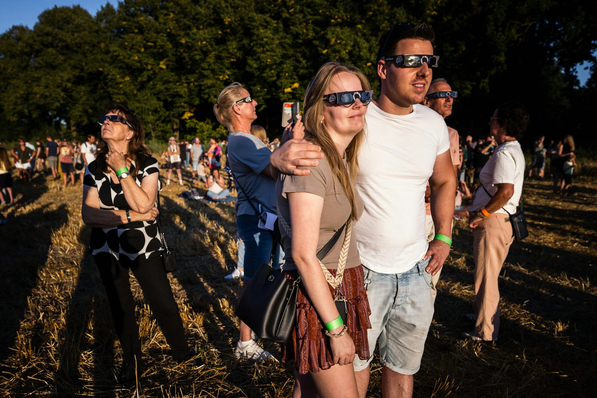 people gather in special glasses to watch the solar eclipse in a field.