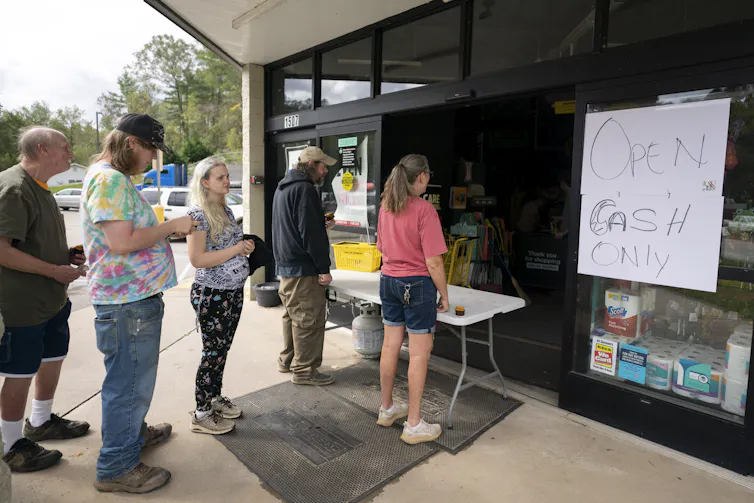 People wait in line outside a Dollar General store. A sign reads 'Open. Cash only.'