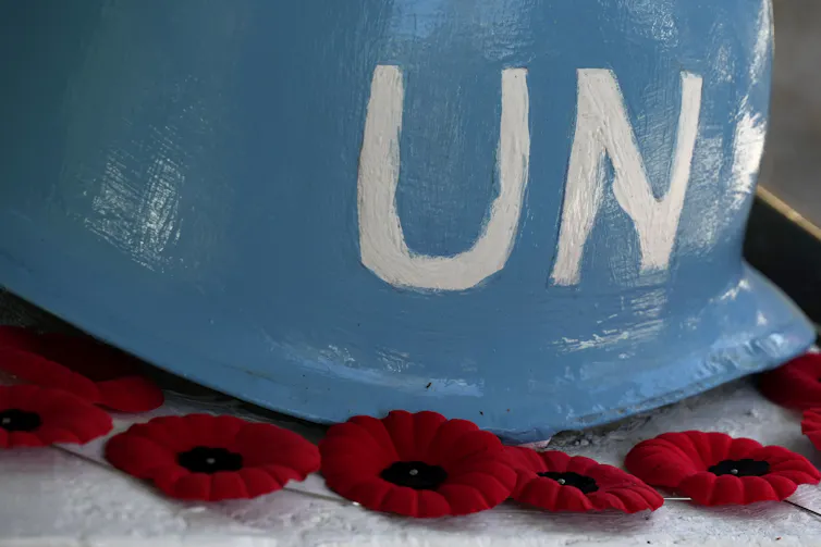 An old blue helmet with UN written on it on top of lapel poppies.