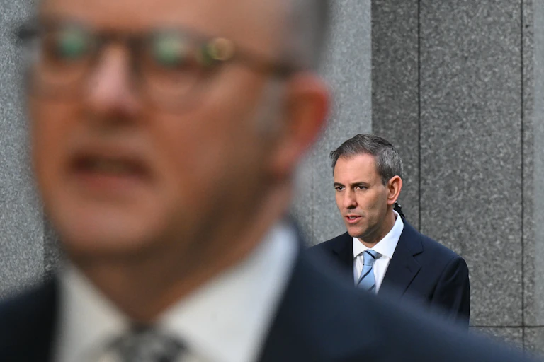 The out of focus face of Anthony Albanese with Jim Chalmers behind him
