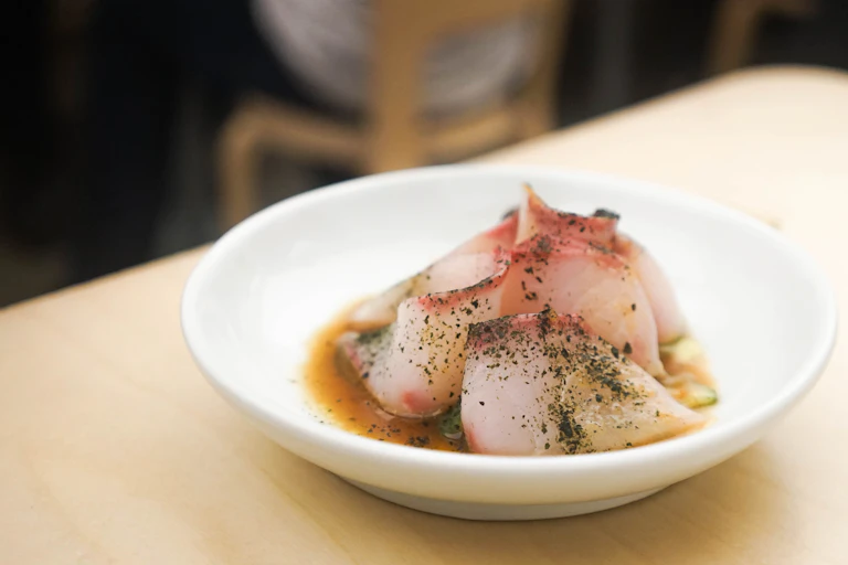 A dish contains several slices of raw kingfish served as sashimi.