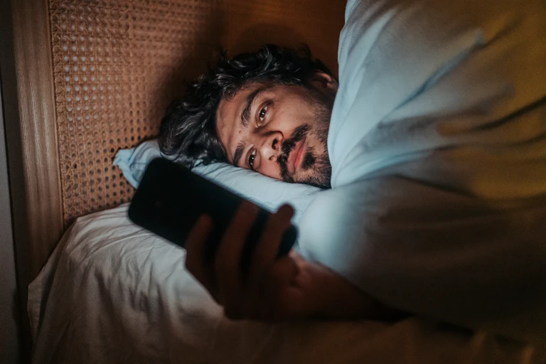 Man lying in bed in the dark looks at his phone.