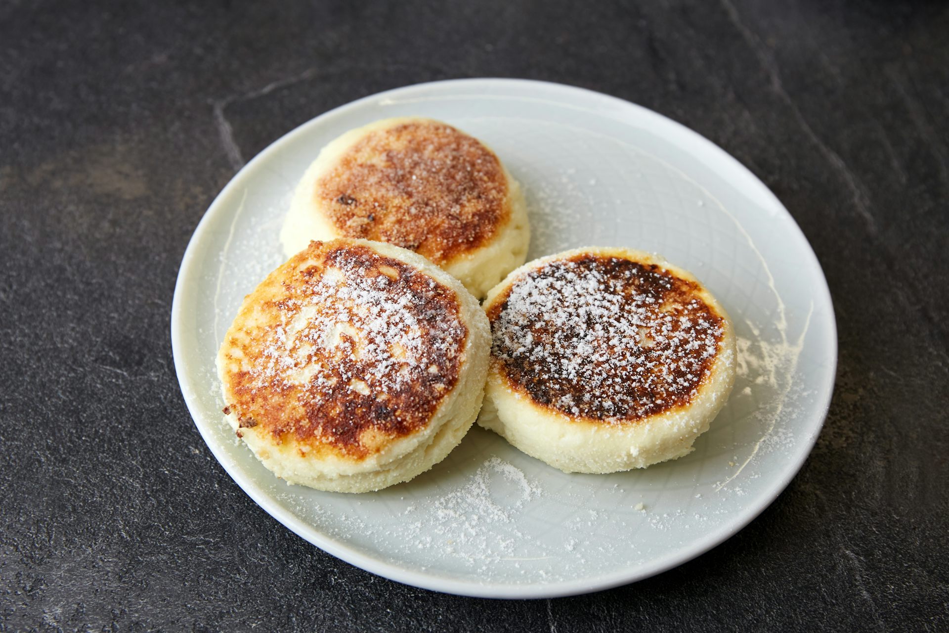 Three pancakes made with cottage cheese sitting on a plate that is dusted with icing sugar.
