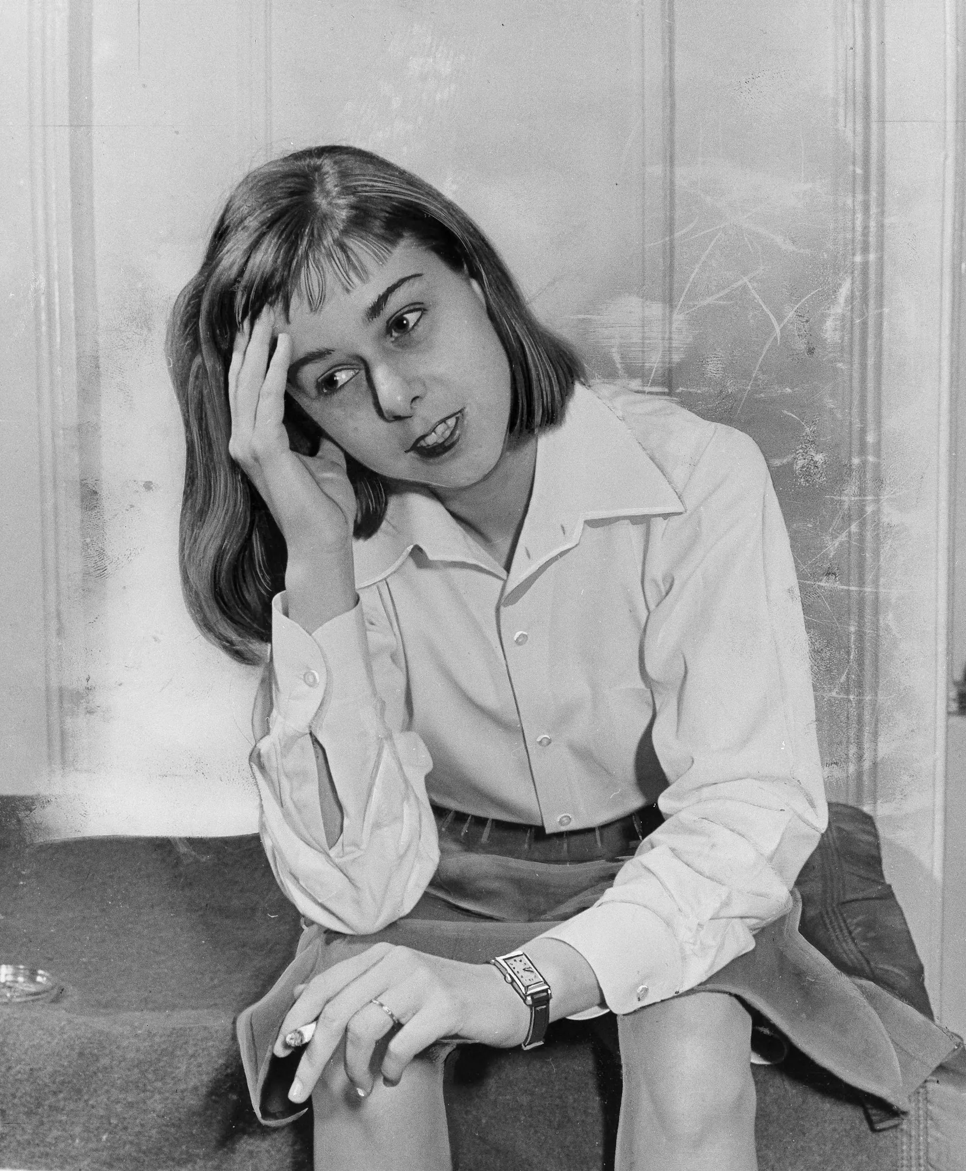 Black and white photo of a young woman sitting a stoop, resting her head in one hand while cradling a cigarette in the other.
