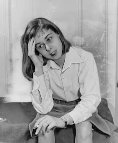 Black and white photo of a young woman sitting a stoop, resting her head in one hand while cradling a cigarette in the other.