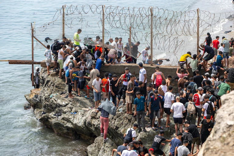 Dozens of people breach barbed wire on a beach.