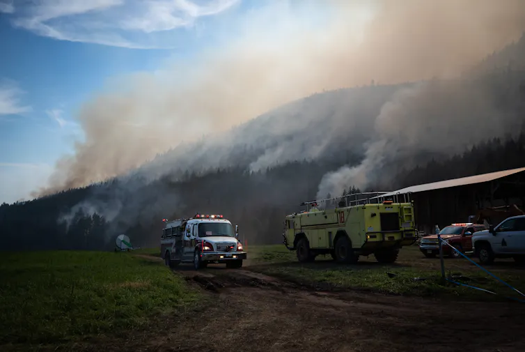 fire trucks on a farm field, smoke rises from a hill in the background
