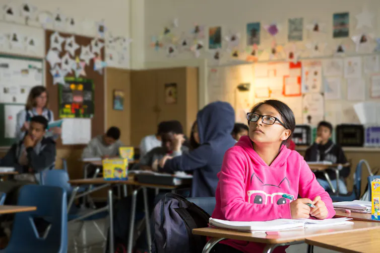 A teenaged student sits in a class with a pensive look on their face.