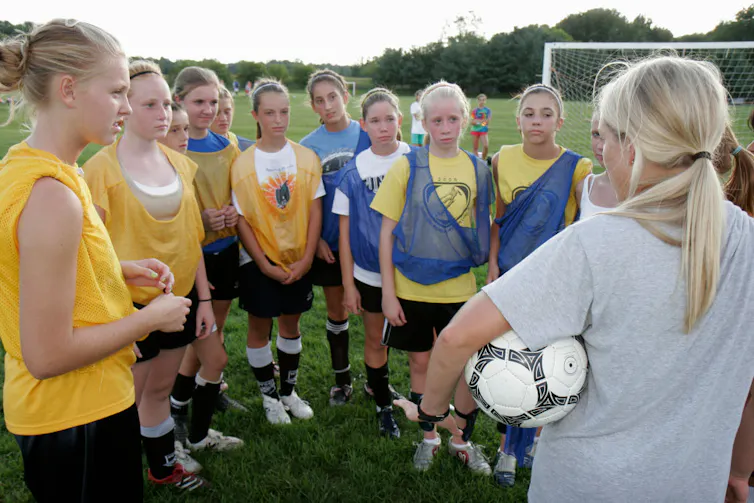 A group of girls on a soccer team listen to their coach.