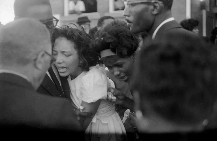 A black and white picture of two men embracing two weeping women.