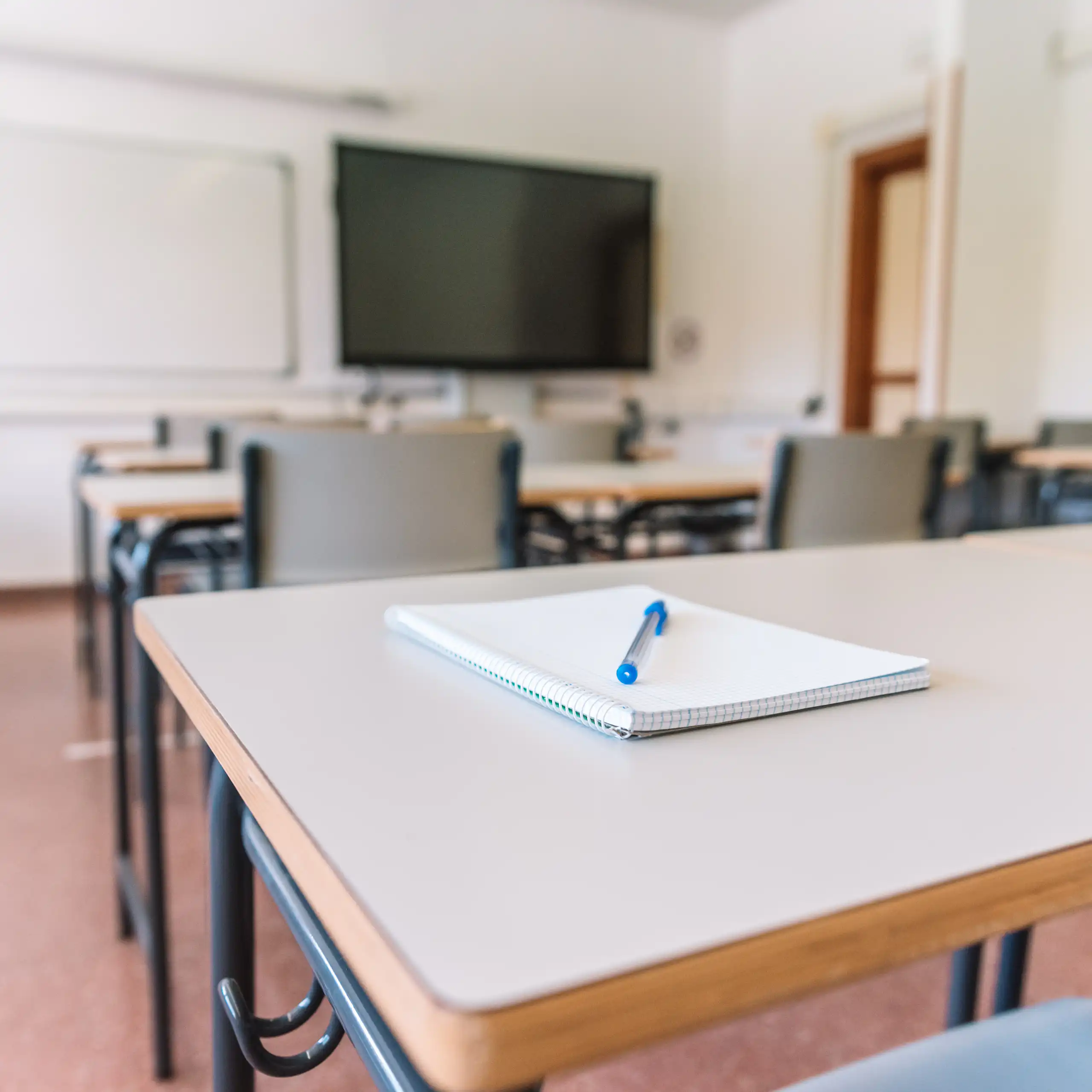 A blank pad of paper and a pen rest on a table in an empty classroom.