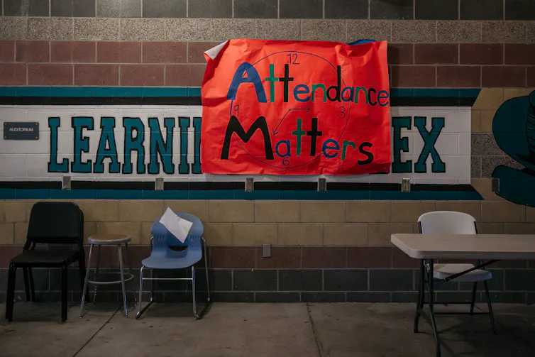 A hand-drawn red sign that says 'Attendance matters' is hung on a tile wall with chairs nearby.