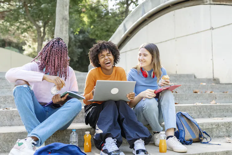 Three young people sit on steps together and smile.