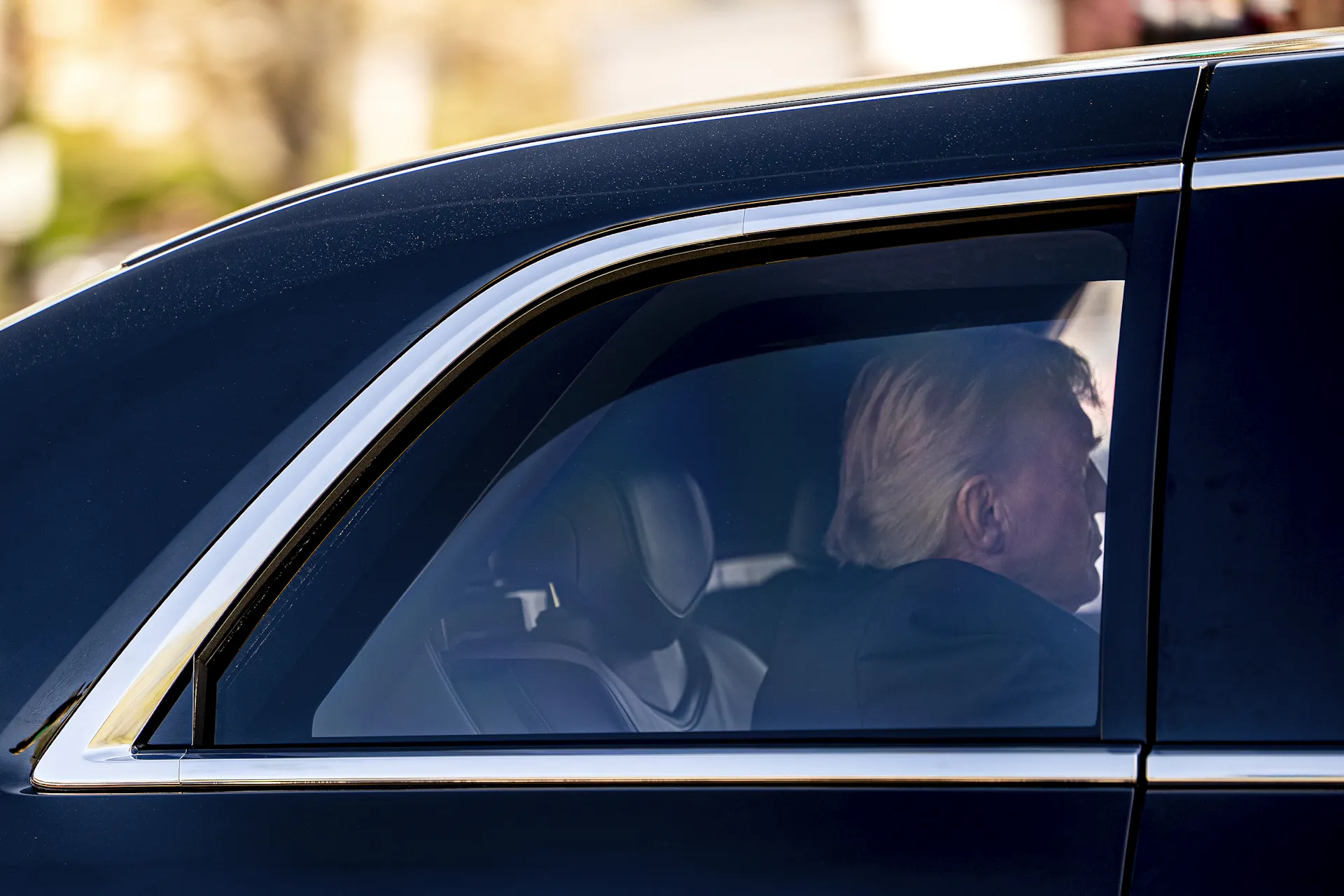 A man sits in the back seat of a black limousine.