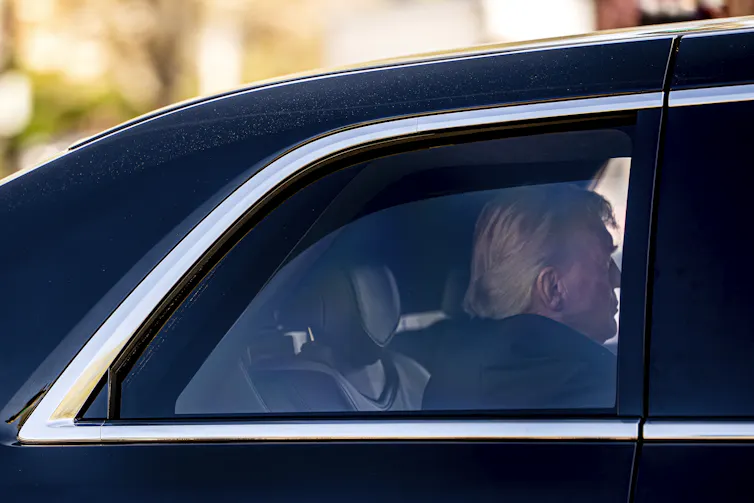 A man sits in the back seat of a black limousine.