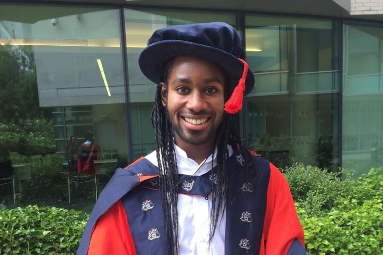 A smiling young man has a blue cap with a red tassel hanging down from the left of his cap