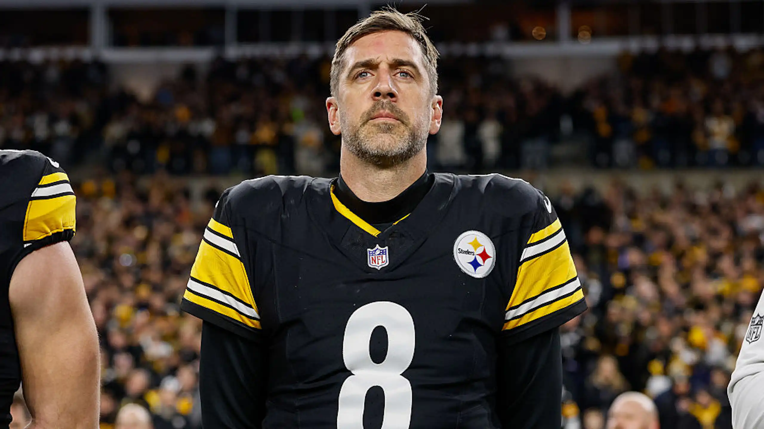 Aaron Rodgers, wearing his Steelers jersey, stands on a field.