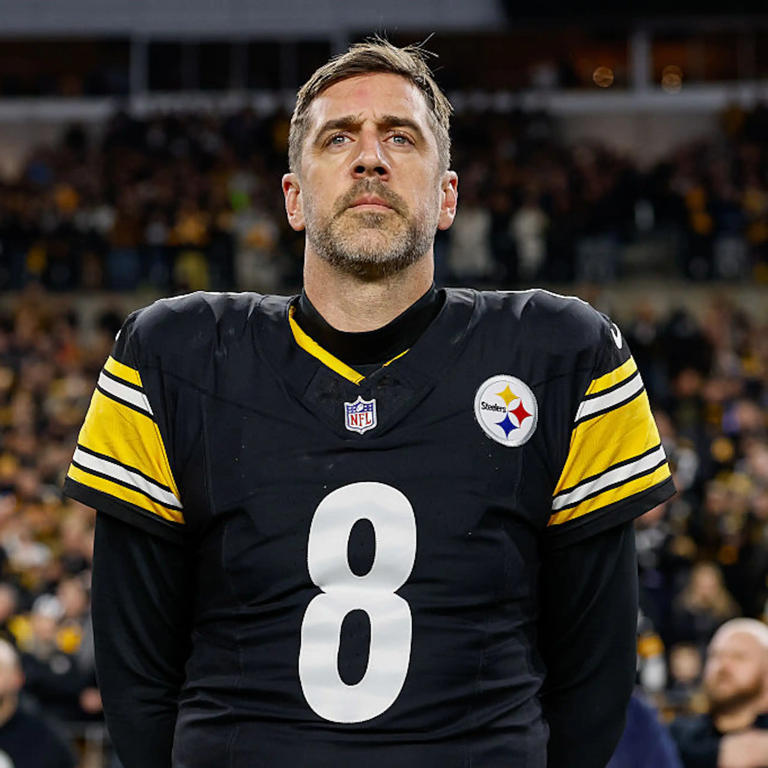 Aaron Rodgers, wearing his Steelers jersey, stands on a field.