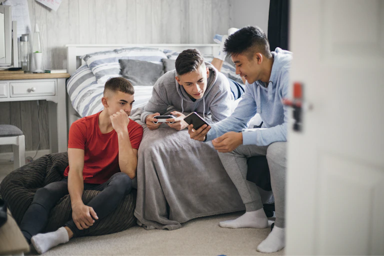 A group of teen boys look at a smartphone in a bedroom