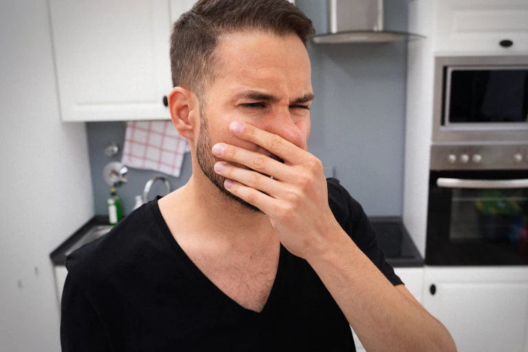 A man holds his nose while standing in a staff kitchen.