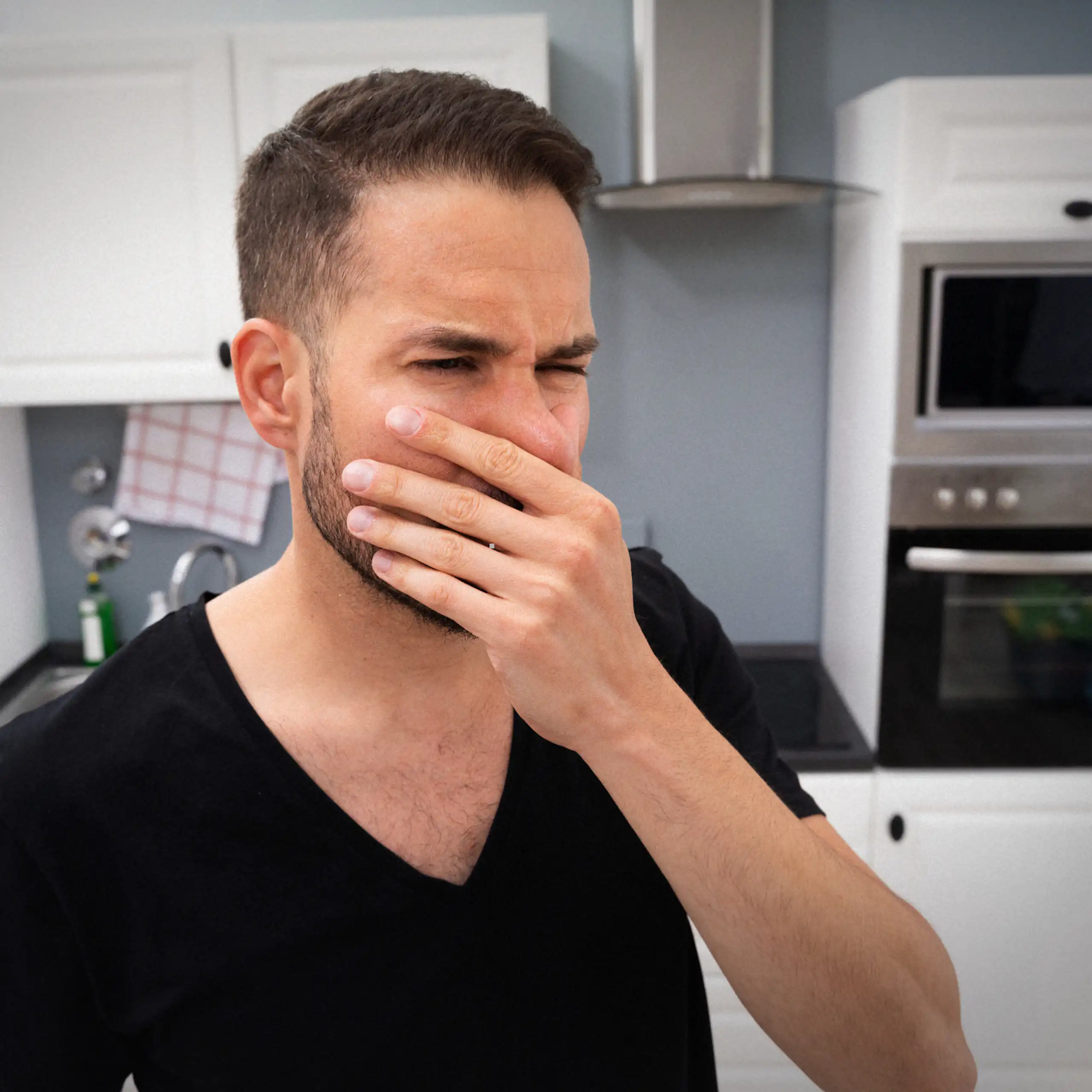 A man holds his nose while standing in a staff kitchen.