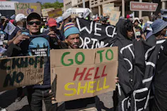People march with one holding a placard saying 'Go to Hell, Shell'