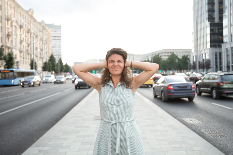 A woman covers her ears in the middle of the streets of a city