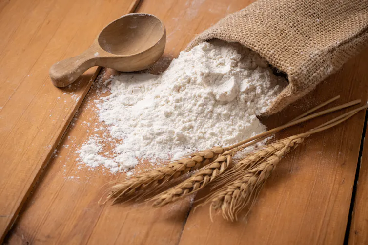 A bag of white flour which has spilled onto a table.