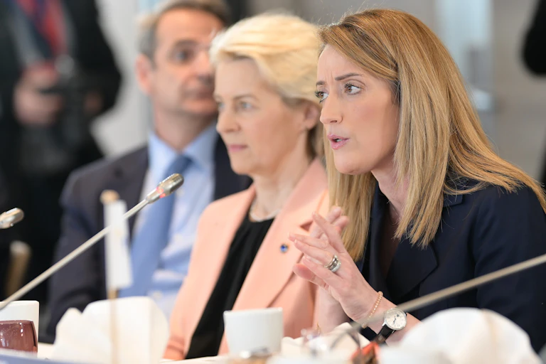 Roberta Metsola speaking into a microphone at a table, with Ursula von der Leyen sitting to her right