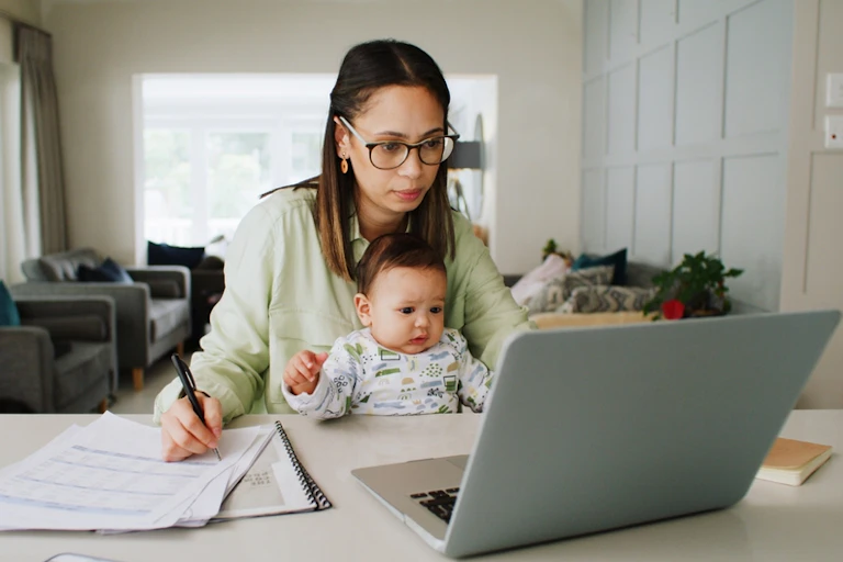 Women with baby sitting at desk in front of laptop