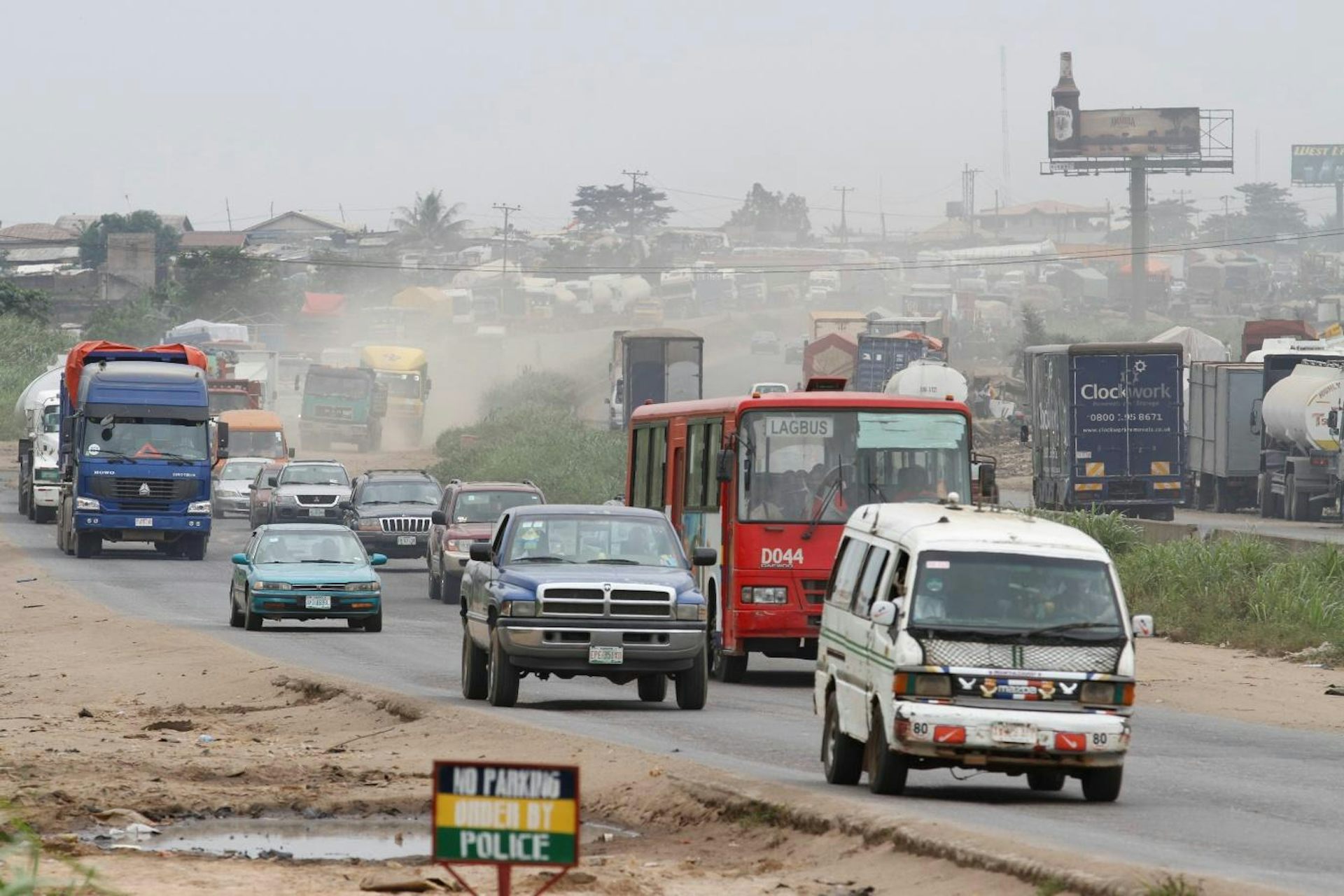 Cars, buses and trucks on a busy road with a pool of muddy water next to it.