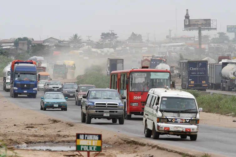 Cars, buses and trucks on a busy road with a pool of muddy water next to it.