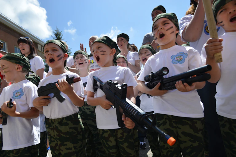 Photo de groupe d'enfants en train de chanter et portant des jouets en forme de mitraillette, le visage grimé comme des soldats de commando.