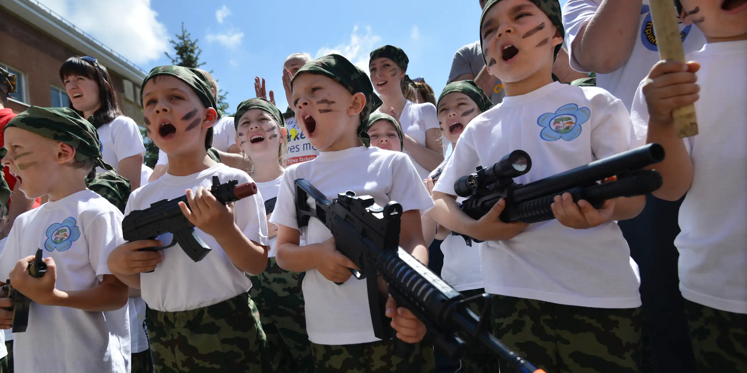 Photo de groupe d'enfants en train de chanter et portant des jouets en forme de mitraillette, le visage grimé comme des soldats de commando.