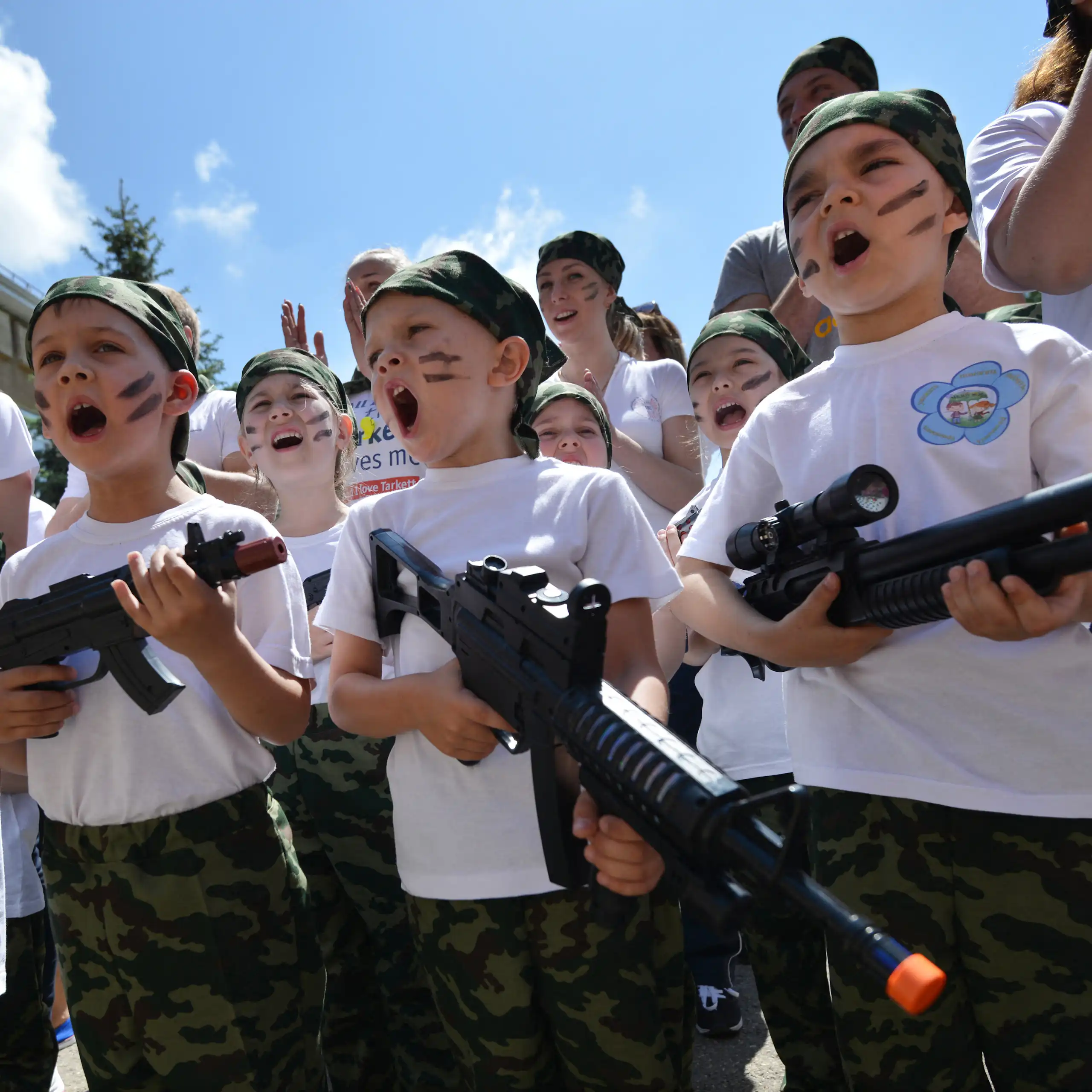 Photo de groupe d'enfants en train de chanter et portant des jouets en forme de mitraillette, le visage grimé comme des soldats de commando.