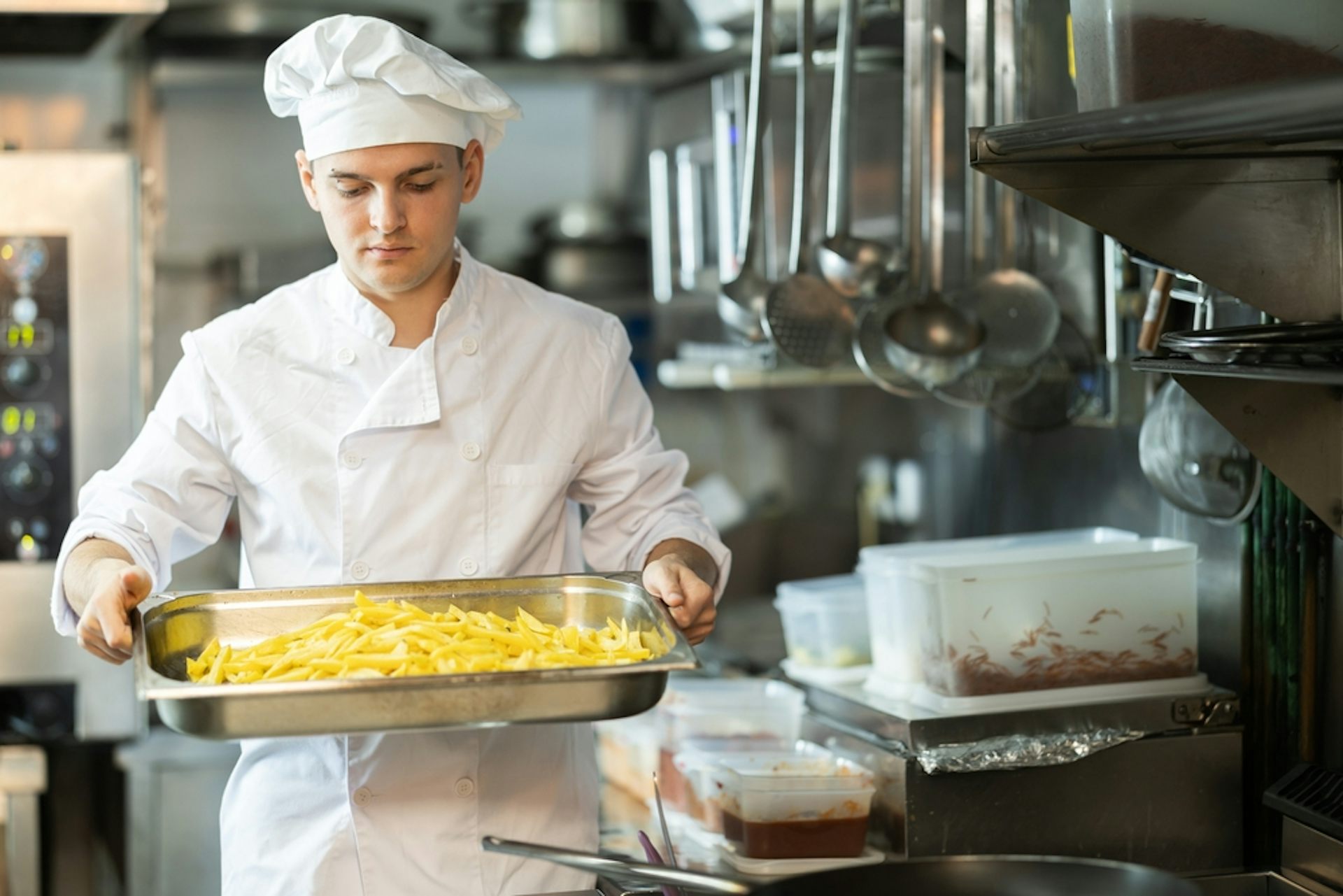 A young chef carries a tray of fires in a kitchen
