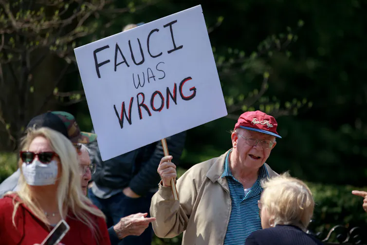 A man wearing a red hat holds a sign that reads 'Fauci was wrong.'