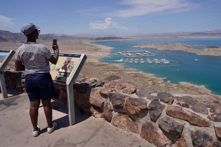 A person stands at an overlook, from which a lake is visible in the distance, with a wide dry area all around it.