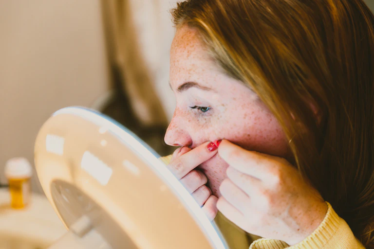 Young woman sitting at make-up mirror, squeezing pimple