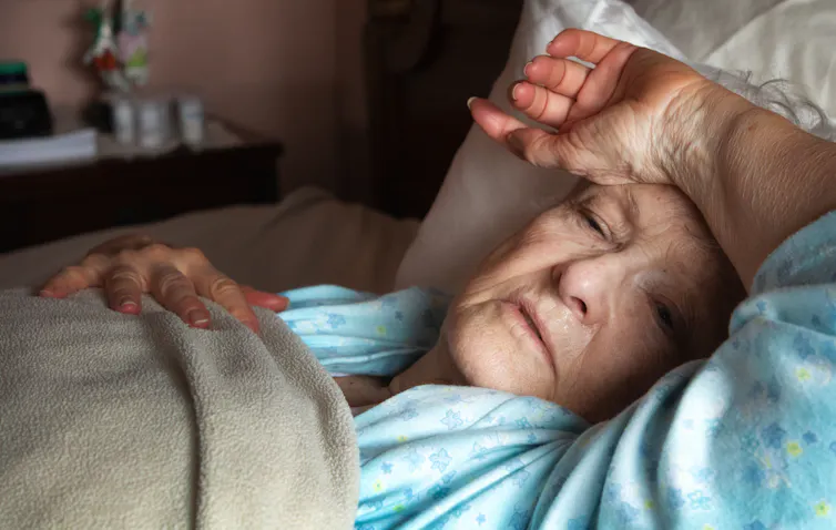 An older woman lays in bed, sick with COVID